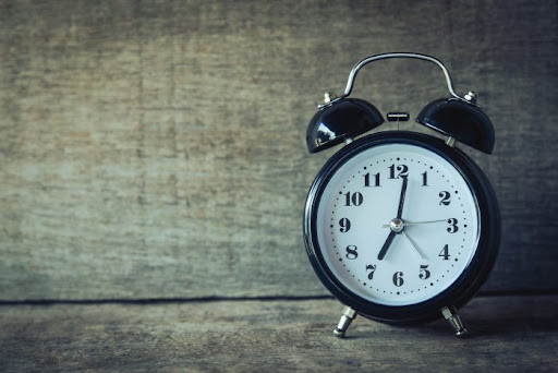 ένα μαύρο ξυπνητήρι με δείκτη χρόνου 7:00, τοποθετημένο πάνω σε ξύλινο επιφάνεια.
